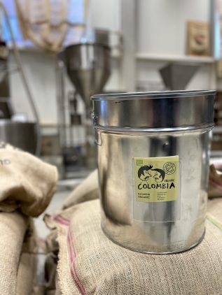 Our organic-certified coffee – Colombia Magdalena, Sierra Nevada ORGANIC. A metal coffee container with a yellow label and the EU organic logo, placed on coffee sacks in a roastery.