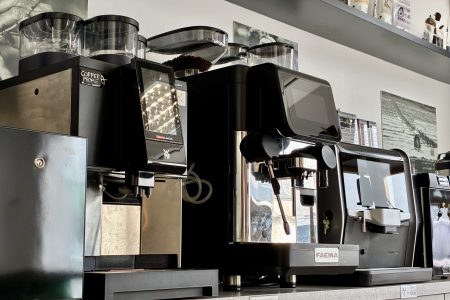 Coffee People kohvimasinad ja kohviveski professionaalses kohviröstikojas – esiplaanil FAEMA, WMF ja Duke de Jong espressomasinad, taustal eritooted ja kohvipakid riiulil.
