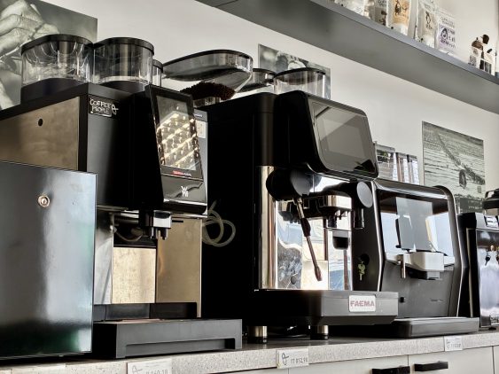 Coffee People kohvimasinad ja kohviveski professionaalses kohviröstikojas – esiplaanil FAEMA, WMF ja Duke de Jong espressomasinad, taustal eritooted ja kohvipakid riiulil.