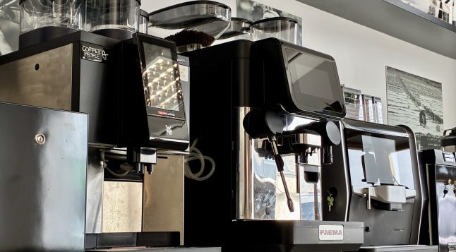 Coffee People kohvimasinad ja kohviveski professionaalses kohviröstikojas – esiplaanil FAEMA, WMF ja Duke de Jong espressomasinad, taustal eritooted ja kohvipakid riiulil.